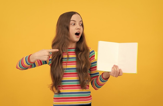 Petite fille surprise pointer du doigt un livre ouvert pour copier l'espace fond jaune pointant