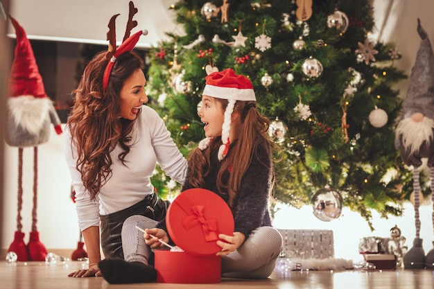 Une petite fille surprise regarde le cadeau dans la boîte rouge qu'elle vient de recevoir de sa mère.