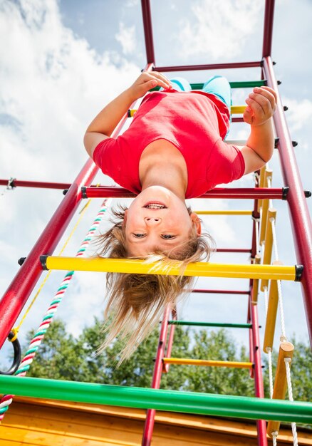 Petite fille suspendue à un gymnase de jungle jouant dans un jardin d'été enfant concept de jeu risqué