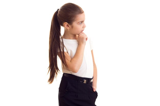 Petite fille sympa avec une longue queue de cheval brune en T-shirt et jupe noire sur fond blanc en studio