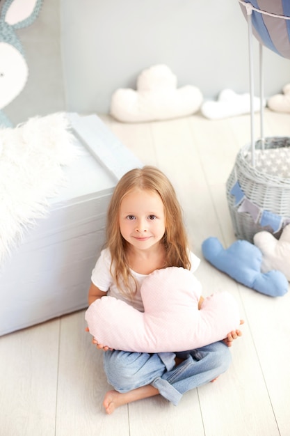 Une petite fille en T-shirt et jeans tient un oreiller nuage contre le mur d'un ballon décoratif. Tout-petit joue dans la chambre des enfants. Le concept d'enfance, de voyage. Salle intérieure