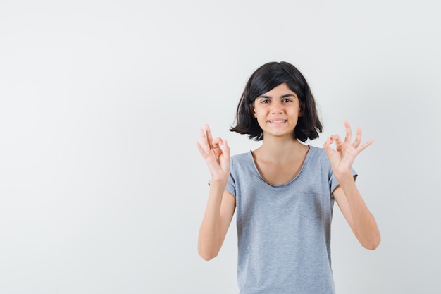 Petite fille en t-shirt montrant le geste ok et à la joyeuse, vue de face.