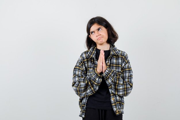 Petite fille en t-shirt, veste montrant les mains jointes dans un geste suppliant et l'air plein d'espoir, vue de face.