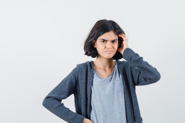 Petite fille en t-shirt, veste se gratter la tête et à la recherche pensive, vue de face.