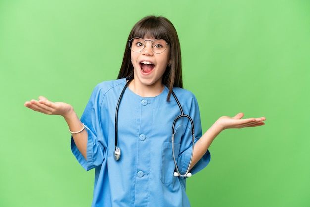 Petite fille en tant que médecin chirurgien sur fond isolé chroma key avec une expression faciale choquée