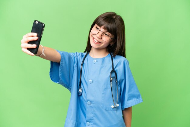 Petite fille en tant que médecin chirurgien sur fond isolé chroma key faisant un selfie