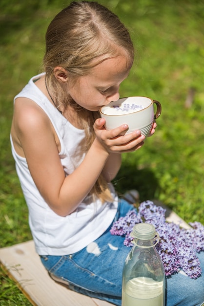 Petite fille avec une tasse de lait sur la nature