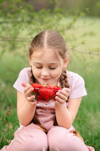 Petite fille tenant une assiette avec des fraises dans la nature Concept de jardinage et d'agriculture Vegan Vertical végétarien
