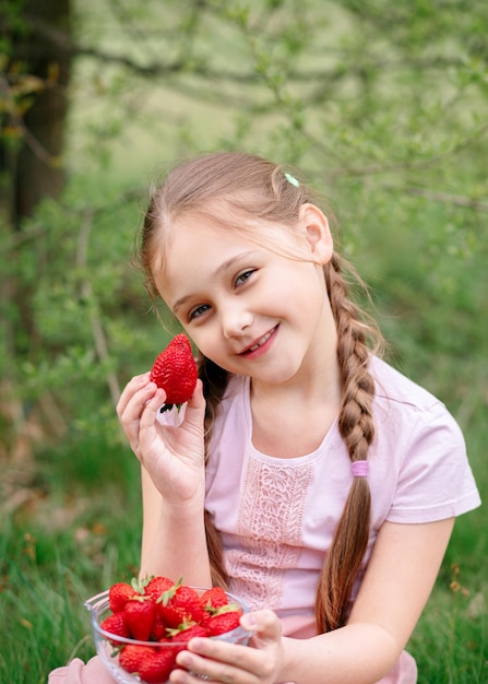 Petite fille tenant une assiette avec des fraises dans la nature Concept de jardinage et d'agriculture Vegan Vertical végétarien