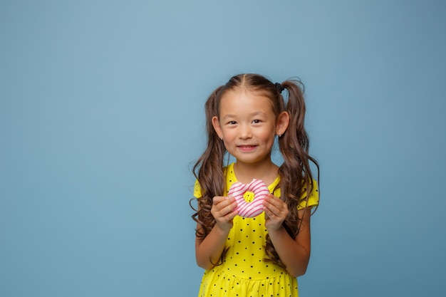 Petite fille tenant un beignet sur fond bleu