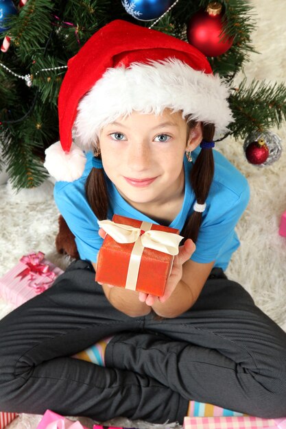 Petite fille tenant une boîte-cadeau près de l'arbre de Noël