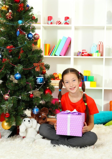 Petite fille tenant une boîte-cadeau près de l'arbre de Noël