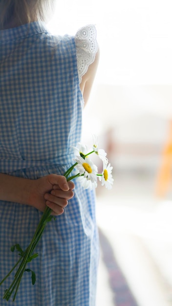 Une petite fille tenant un bouquet de marguerites derrière son dos