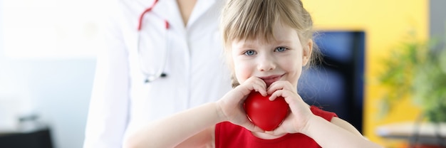 Petite fille tenant un coeur de jouet rouge dans ses mains dans le concept de santé des enfants du bureau des médecins