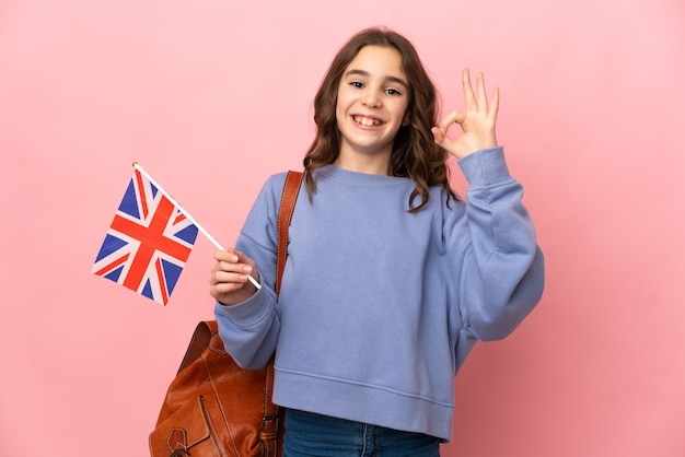 Petite fille tenant un drapeau du Royaume-Uni isolé sur fond rose montrant signe ok avec les doigts