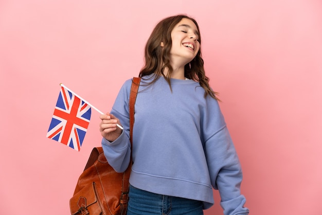 Petite fille tenant un drapeau du Royaume-Uni isolé sur un mur rose en riant