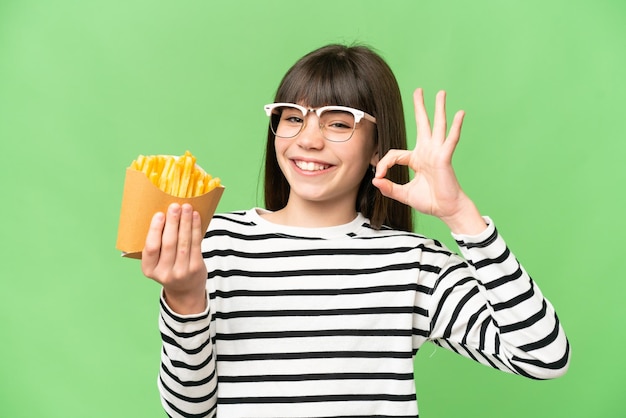 Petite fille tenant des frites frites sur fond de clé chroma isolé montrant un signe ok avec les doigts