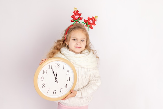 Petite fille tenant une horloge sur fond blanc isolé avec le pull, place pour texte, concept de nouvel an et Noël