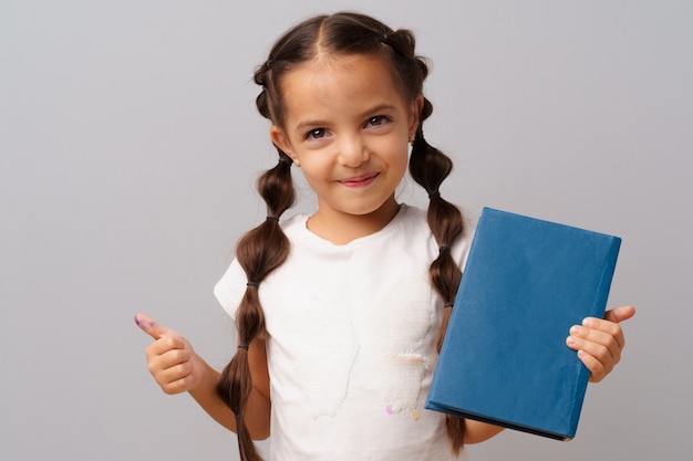 Petite fille tenant un livre dans ses mains sur un fond gris