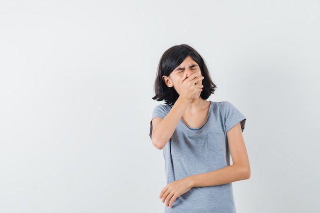 Petite fille tenant la main sur la bouche en t-shirt et regardant triste. vue de face.