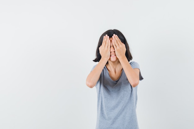 Petite fille tenant les mains sur les yeux en t-shirt et à la recherche d'excitation. vue de face.