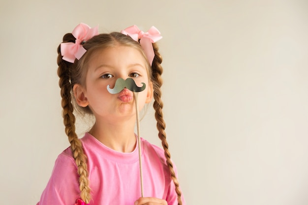 Une petite fille tenant une moustache fantaisie.