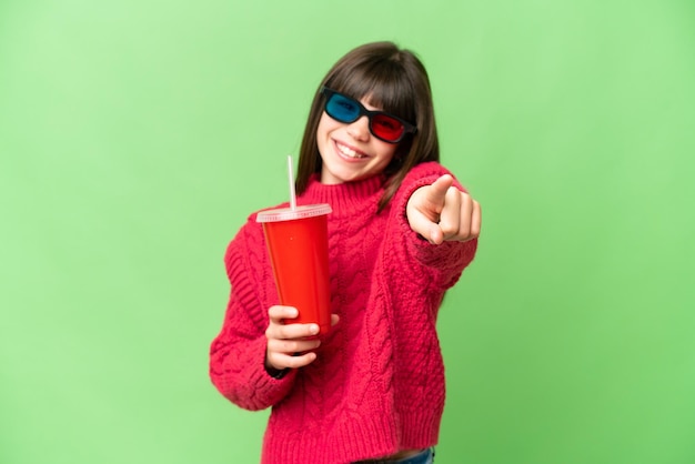 Petite fille tenant un soda sur fond isolé chroma key pointant vers l'avant avec une expression heureuse