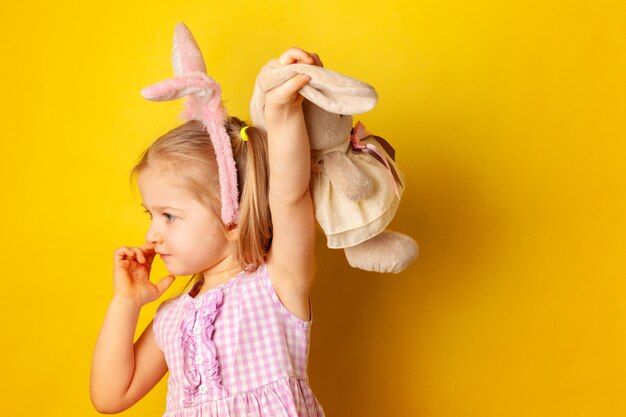 Petite fille tenant son jouet lapin contre une surface jaune