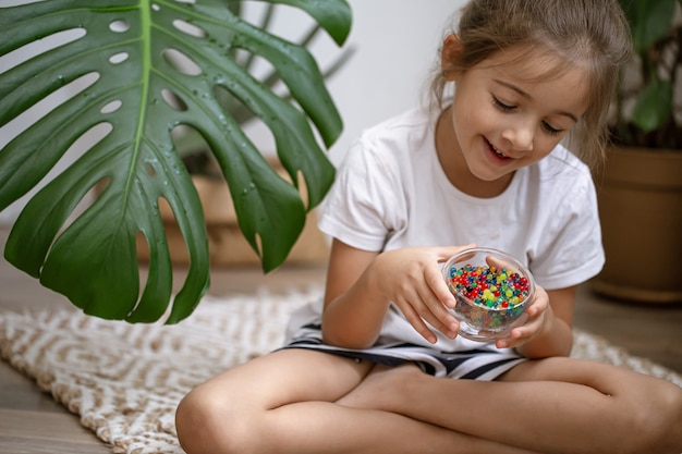 Petite fille tenant un vase avec des perles d'eau multicolores décoratives.