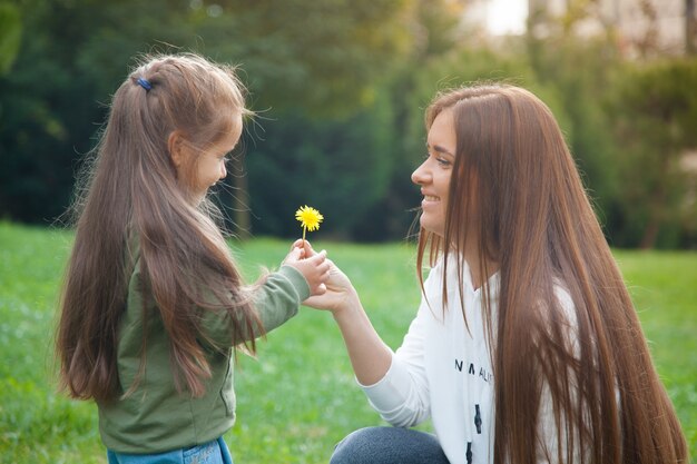 Petite fille tend un pissenlit à sa mère dans le parc. Concept de mère et fille.