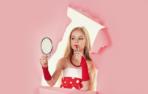 Petite fille tenir le rouge à lèvres. Petit adolescent sur fond rose. Kid avec du maquillage.