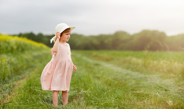 la petite fille sur le terrain tient un chapeau sur la tête et regarde au loin