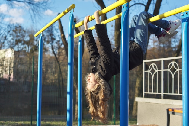 Petite fille la tête en bas sur une aire de jeux de sports en plein air avec les yeux fermés, profitant de la chaleur et de la lumière du soleil, premier soleil du printemps, vitamine D