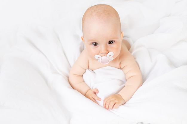 Petite fille avec une tétine dans un berceau sur un lit en coton blanc âgé de six mois