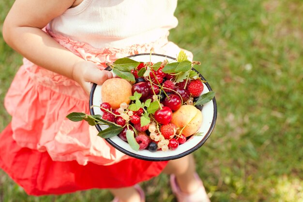 La petite fille tient un bol avec des fruits d'été