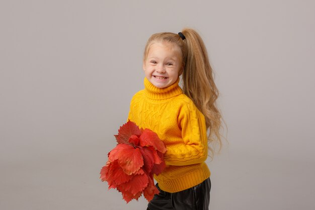 Une petite fille tient un bouquet de feuilles d'automne sur un espace gris