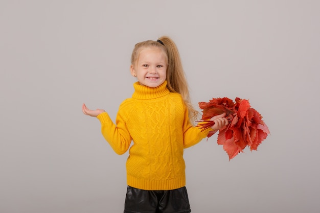 Une petite fille tient un bouquet de feuilles d'automne sur un espace gris