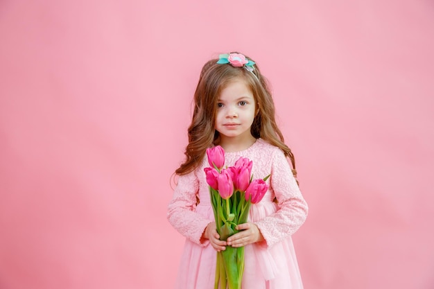 Une petite fille tient un bouquet de tulipes roses sur fond rose