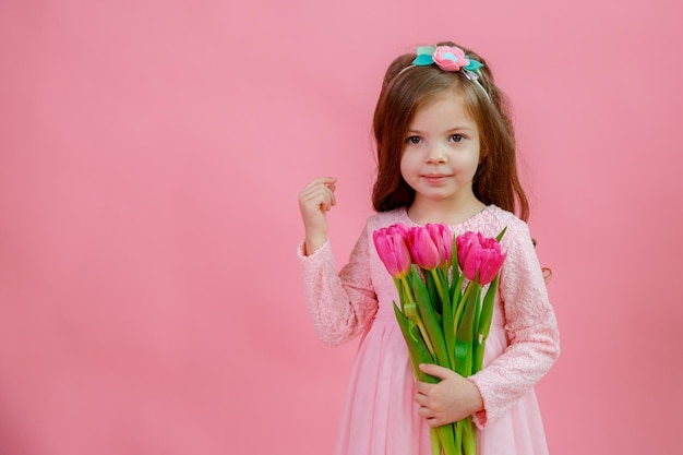 Une petite fille tient un bouquet de tulipes roses sur fond rose