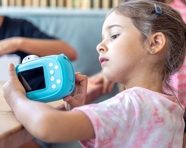 Une petite fille tient dans ses mains un appareil photo numérique jouet bleu pour enfants pour une impression photo instantanée.