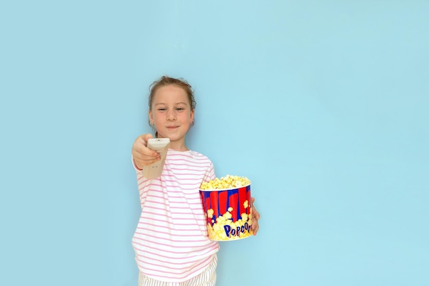 Petite fille tient un grand verre de pop-corn dans une main tout en tenant la télécommande du téléviseur avec l'autre