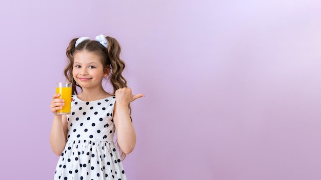 Une petite fille tient un jus d'orange et pointe vers une publicité sur un fond rose isolé Espace de copie