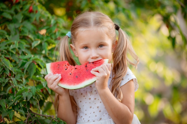 Une petite fille tient un morceau de pastèque au soleil d'été