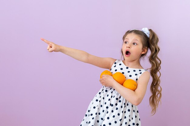 Une petite fille tient des oranges et pointe vers une publicité sur un fond rose isolé