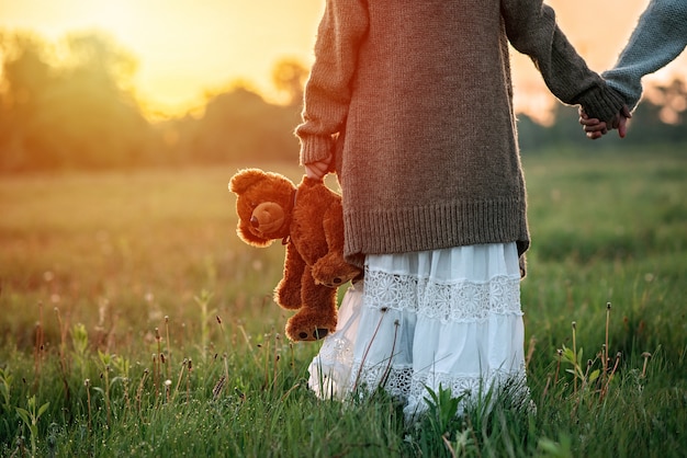 Petite fille tient un ours en peluche dans sa main à l'aube dans l'herbe. Le concept de solitude.