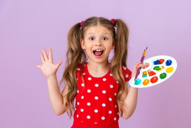 Une petite fille tient une palette de peinture dans ses mains et est très heureuse.