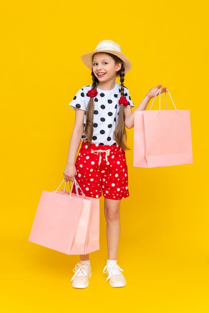 Une petite fille tient des sacs à provisions Un enfant dans un chapeau d'été et un short est engagé dans les achats pour enfants Un enfant heureux en pleine croissance sur un fond isolé jaune