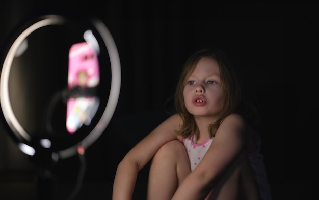 Une petite fille tourne une vidéo sur un trépied dans l'obscurité. Enfant blogueur et plaisir du concept de réseaux sociaux