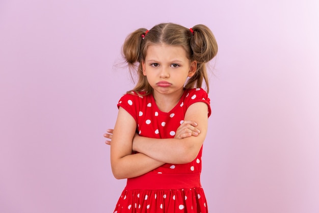 Une petite fille, très offensée et bouleversée. Robe rouge à pois sur fond isolé.