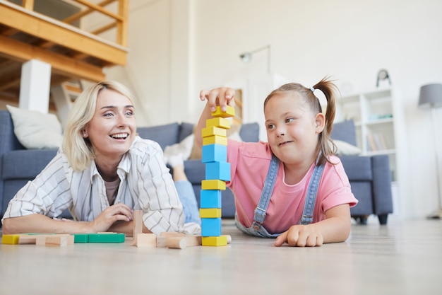 Petite fille trisomique, construire une tour à partir de blocs colorés avec sa mère sur le sol à la maison